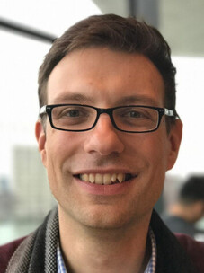 Martin Stehno mit Brille und kurzem Haar, im urbanen Hintergrund.